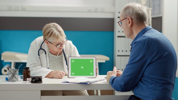 Senior physician pointing at tablet with horizontal greenscreen