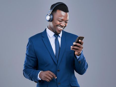 Accessing his favourite playlists. a handsome young businessman using his cellphone to listen to music in studio against a grey background.