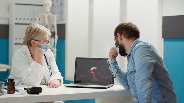 Physician analyzing virus animation on laptop with sick patient