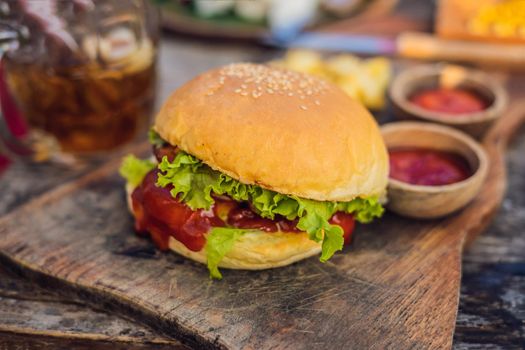 Closeup of fresh burger with French fries on wooden table with bowls of tomato sauce. lifestyle food
