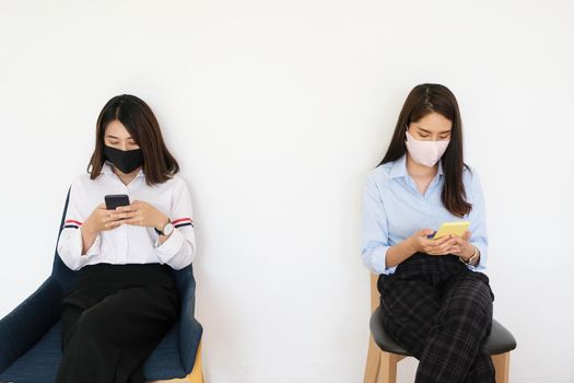 social distancing concept, Two women wearing masks and distancing while sitting on mobile phones following coronavirus social trend.