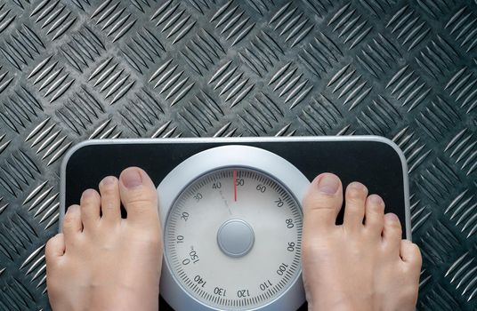 Top view of feet on weighing scale. Women weigh on a weight balance scale after diet control. Healthy body weight. Weight and fat loss concept. Weight measure machine. Body Mass Index or BMI concept.