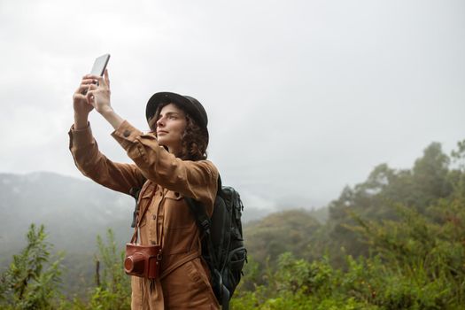 Female tourist with a backpack taking a selfie while hiking in the mountains