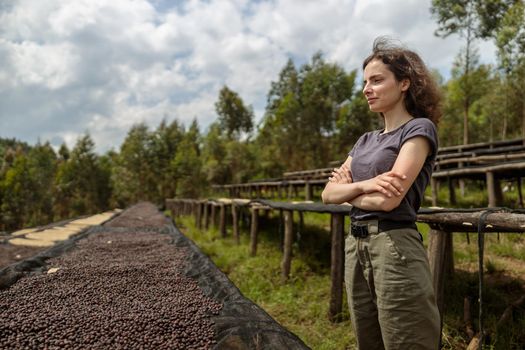 Pretty lady with arms crossed standing near tables of drying coffee beans