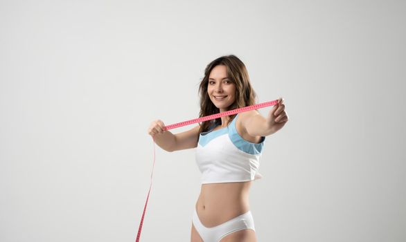 Happy sexy brunette fitness woman with pink measure tape before measuring her waistline on white background. Time for diet and slimming weight loss. Health care and healthy nutrition.