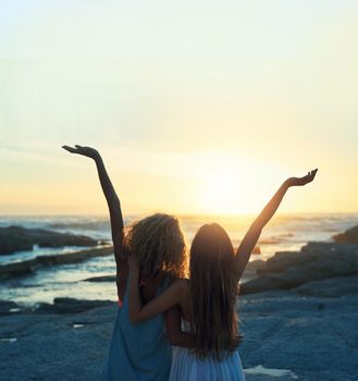 two woman friends on beach celebrating with arms raised looking at sunset enjoying travel freedom lifestyle.