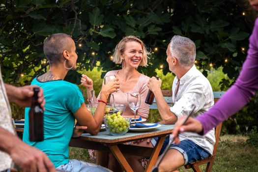 Adult friends laugh and talk outdoors during garden dinner party.