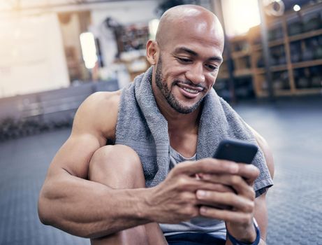 Lets see if any of my buddies wanna hangout. a muscular young man using a cellphone while taking a break from exercising in a gym.