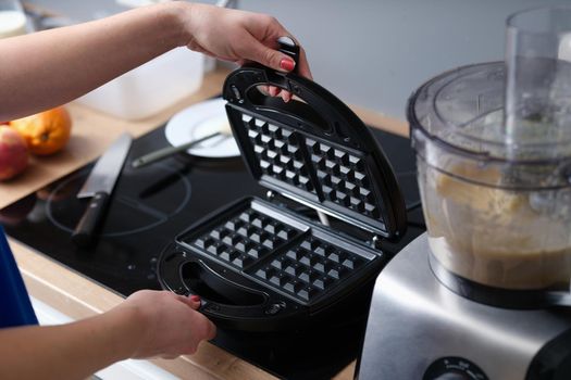 Woman has prepared Belgian waffle dough and opens electric waffle iron