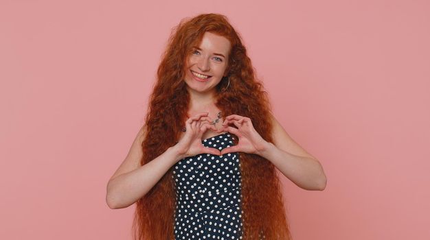 Smiling ginger girl makes heart gesture demonstrates love sign expresses good feelings and sympathy
