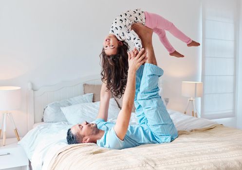 Wake up and have a fun-filled day. a man lying on a bed and lifting his daughter in the air with his feet.
