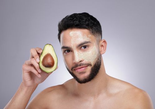 A powerful multipurpose ingredient. a young man holding the avocado used to make his face mask against a studio background.