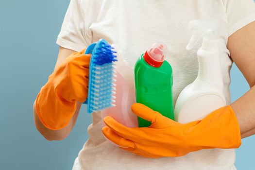 Woman holding bottles of washing liquid and a brush on a blue background.