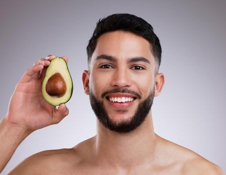 Avocado tends to be deeply hydrating. a young man holding an avocado against a studio background.