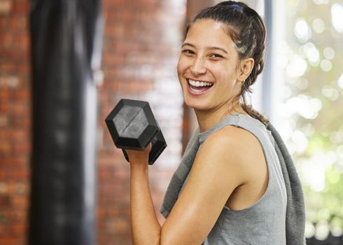 Working for that toned body. Portrait of a sporty young woman exercising with a dumbbell in a gym.