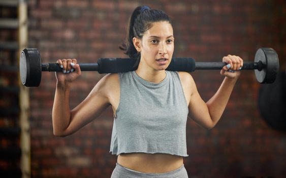 Getting into the best shape. a sporty young woman exercising with a barbell in a gym.