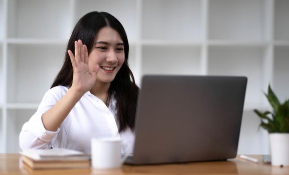 Pretty and charming young Asian female employee having a video call with her team via laptop computer. Remote working concept