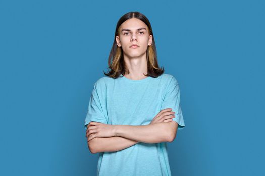 Portrait of serious teenage guy looking at camera on blue background