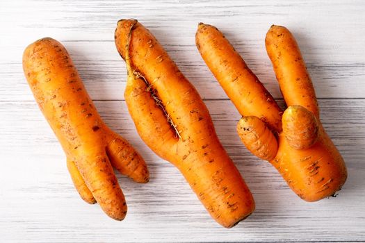 Several ripe orange ugly carrots lie on a light wooden surface
