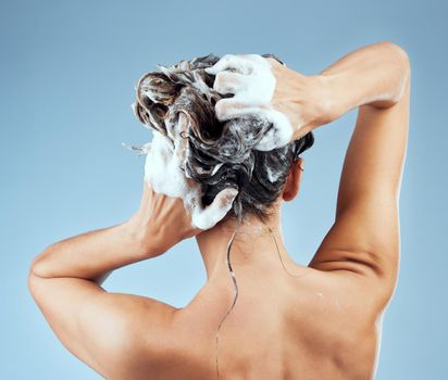 Frizzy hair days are not a thing for her. Studio shot of an attractive young woman washing her hair while taking a shower against a blue background.