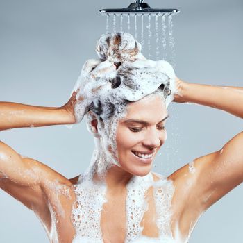 She makes her hair a priority. a young woman washing her hair in the shower against a grey background.
