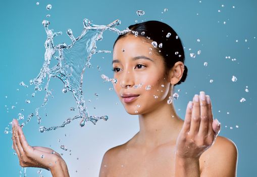 The skin needs extra moisture as we age. an attractive young woman posing against a blue background in the studio and splashing her face with water.