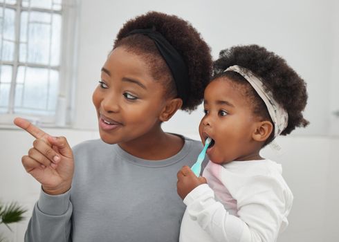 Do you see how clean your teeth are in the mirror. a mother helping her little daughter brush her teeth in the bathroom at home.
