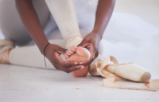 Yet, we dance on. an unrecognizable ballet dancer tying on her pointe shoes.