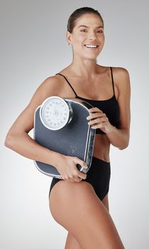 Scale down on bad food, beef up on the good. Studio shot of an attractive and fit young woman holding a scale against a grey background.