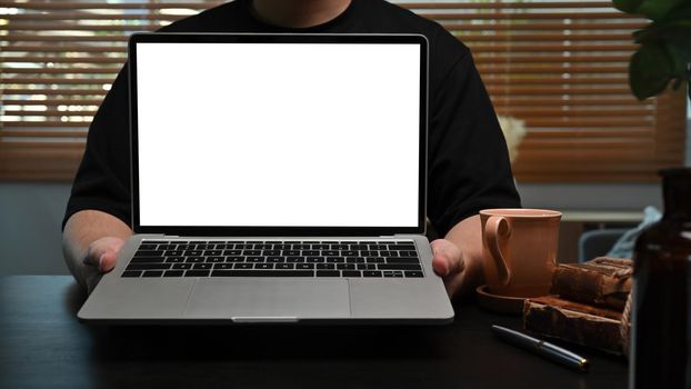 Young man holding mock up computer laptop with blank screen.