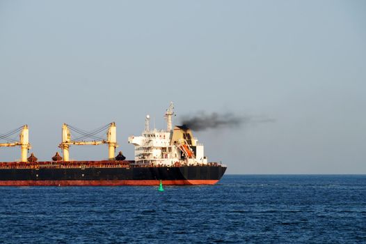 Cargo ship with black smoke from the chimney on the sea horizon close-up