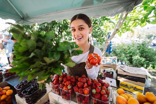 Young saleswoman at work, holding parsley and tomato in hands
