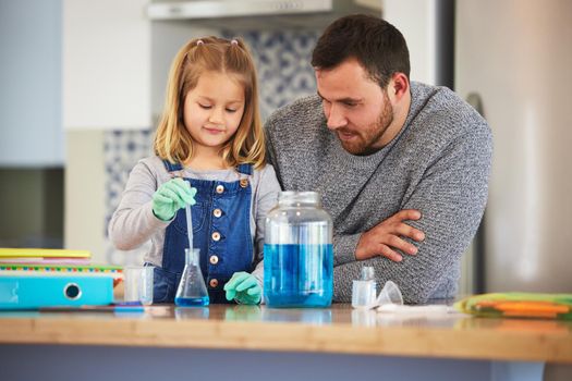 The liquid should change colour. a little girl completing scientific experiments with her dad at home.