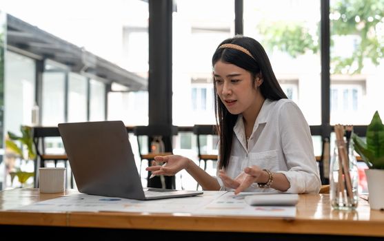 Young asian woman having conference video call using laptop talking to coworker online audience. Consultation, webinar, tutoring on internet, telecommuting