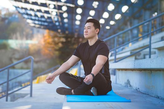 handsome asian man meditating in modern urban stadium, sitting lotus pose