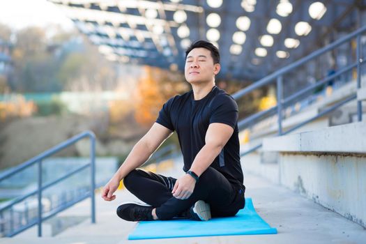 handsome asian man meditating in modern urban stadium, sitting lotus pose