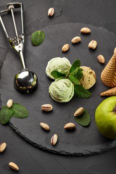 Delicious pistachio and chocolate ice cream decorated with fresh mint and served on a stone slate over a black background.