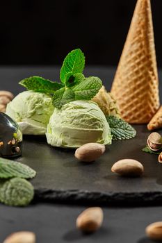 Delicious pistachio ice cream decorated with fresh mint and served on a stone slate over a black background.