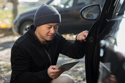 male bandit thief car thief asian uses a tablet to turn off the car alarm
