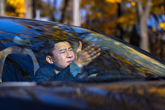 Furious angry asian man standing in a traffic jam beeps and hurries. Sitting in the car.