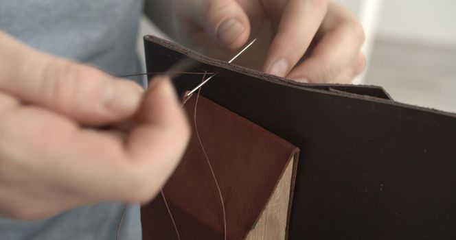 Working process of stitching a brown leather wallet by needle in the leather workshop.