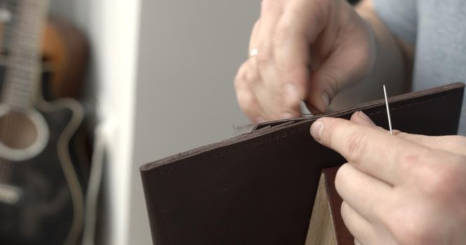 Man working with leather by needle. Genuine Leather. Sewing a purse. Leather work. Tools for sewing bags, wallets, clutches. Stitching. Manual sewing of the product.