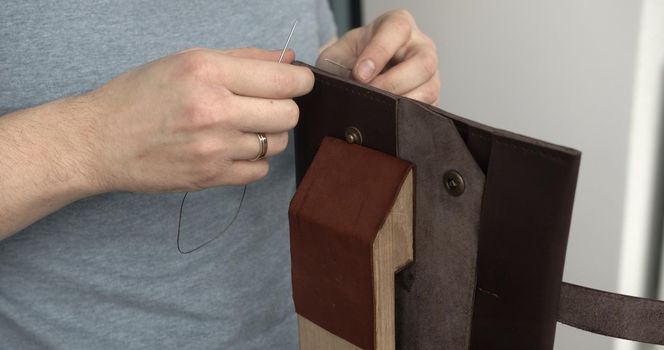 Man working with leather by needle. Tools for sewing bags, wallets, clutches. Stitching.