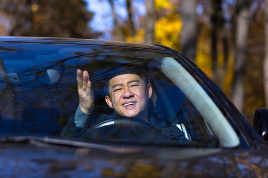 Furious angry asian man standing in a traffic jam beeps and hurries. Sitting in the car.
