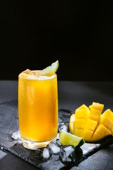 Mango juice on a dark background. Summer drink with ice and slices of mango and lime.