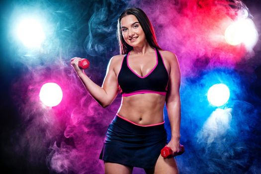 Size plus fitness woman athlete and bodybuilder holding dumbbell on black background with lights and smoke.