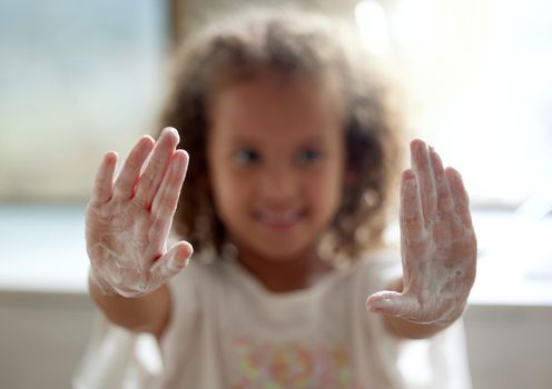 Clean, hygiene and protection from infection by a little girl washing hands with foam soap. Portrait of a child showing soapy palms with sanitizer for virus and germ prevention