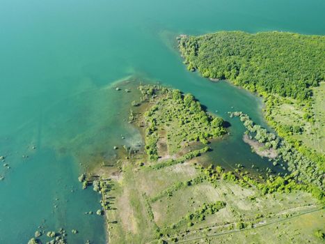 Aerial view on water reservoir at mountain valley covered with green spring forest. Beautiful view from above on smooth blue surface of mountain lake among highlands. Drone point of view. Nobody