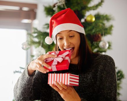 . a young woman opening presents during Christmas at home.