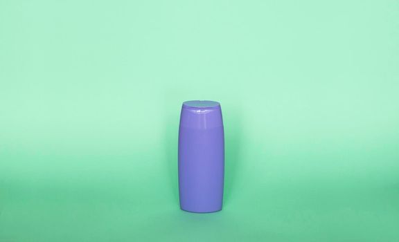 Violet plastic bottle of body care and beauty products. Studio photography of plastic bottle for shampoo, shower gel, creme isolated on green background.